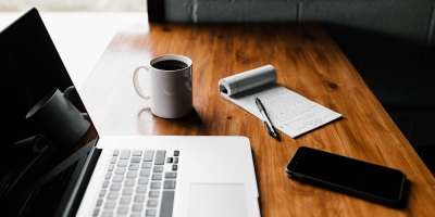 Laptop, coffee mug, notebook and phone on desk